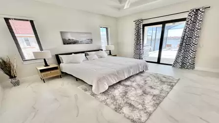 Modern primary bedroom with king-size bed, direct patio access, and stunning waterfront view.