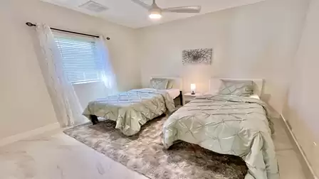 Guest Bedroom 3 features two comfortable twin beds, a bedside table with lamp, and modern curtains