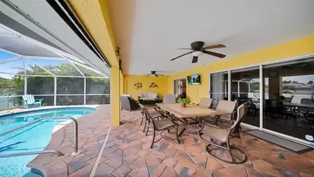 Covered outdoor area with large dining table, ceiling fans, cozy seating and view of the pool and canal – perfect spot for al fresco dining.