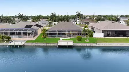 Aerial view of the vacation villa with spacious pool area and direct lakefront location – manicured lawn, palm trees, and a peaceful neighborhood.