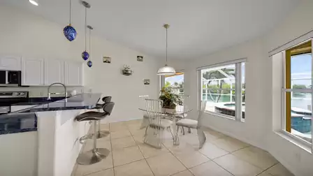 Breakfast area with modern glass table, comfortable chairs and large panoramic window overlooking the pool and lake.