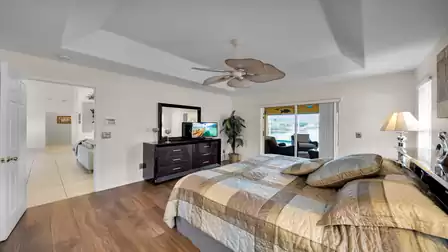 Large master bedroom with elegant ceiling fan, warm wooden flooring and direct access to the covered terrace