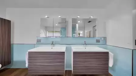 Modern bathroom with double sinks, large mirrors, and elegant wood finishes combined with light blue tiles.