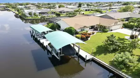 Canal-front property with covered boat lift and lush tropical landscaping.