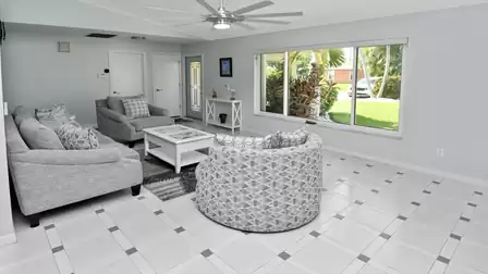 Spacious living area in soft tones with stylish decor and a view of the lush tropical front yard.