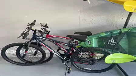 Two mountain bikes stored in a garage next to a green kayak, ready for active outdoor holidays and adventures.
