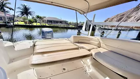 Rear seating area of the motorboat with sun pad and bench, overlooking the canal and palm trees.