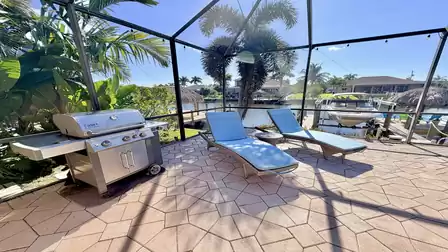 Sun deck with BBQ grill, comfortable loungers and canal views inside a screened patio surrounded by palm trees.