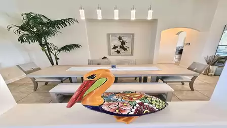 Stylish dining area with large table, modern pendant lights and a decorative pelican sculpture as a focal point.