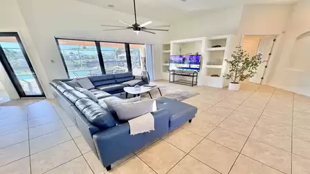 Bright living room with large sectional sofa, TV, ceiling fan and direct access to the terrace and pool area.