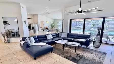 Spacious living area with modern sectional sofa, ceiling fan and open kitchen, featuring views toward the terrace.