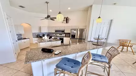 Open kitchen with large island, bar stools, granite countertops, pendant lights and modern appliances.