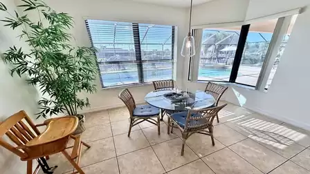 Cozy breakfast nook with round glass table, wicker chairs and plenty of daylight overlooking the pool and patio.