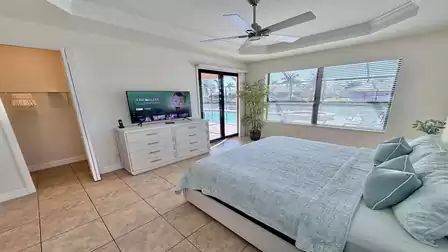 Spacious bedroom with king-size bed, TV, ceiling fan, and sliding doors leading to pool and canal area.