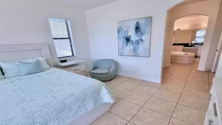 Calm bedroom with king-size bed, reading chair, and direct access to an open en-suite bathroom 