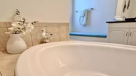 Detail of the bathtub with nice decor and a comfy bench in the bright bathroom.