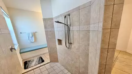 Large walk-in shower with natural tiles, storage shelf, and built-in bench in the bathroom.