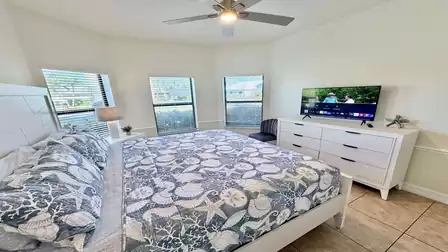 Bright bedroom with king-size bed, TV, ceiling fan, and multiple windows for plenty of natural light.