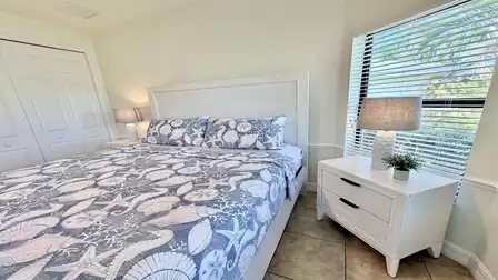 Cozy bedroom with king-size bed, coastal-style bedding, bedside tables, and window overlooking greenery.