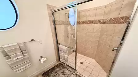 Glass walk-in shower with beige tiles, rainfall showerhead, round window, and towel rack in a bright bathroom.