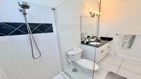 Modern bathroom with walk-in shower, glass panel, granite vanity, and bright, clean lighting.