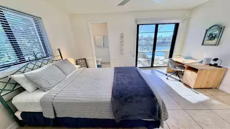 Bedroom with queen size bed, desk, and sliding doors opening to the terrace with pool and water view.