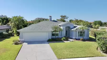Front view of Villa Amagalla in Cape Coral with driveway, well-kept garden and palm trees under a blue sky.