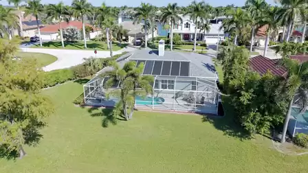 Aerial view of the rear of the house with screened pool, palm trees and a spacious garden in a quiet neighborhood.