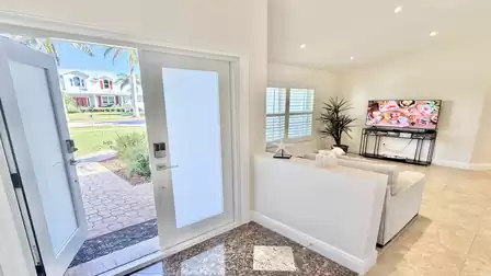 View from the entrance into the bright living room with open front door, sofa, TV and plenty of natural light.