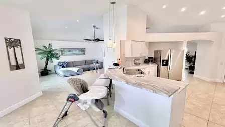 Open kitchen with breakfast bar, bar stools and view into the living area with sofa and ceiling fan.