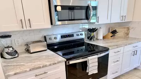Kitchen detail with ceramic cooktop, microwave, light cabinets and modern countertop.