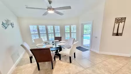 Bright dining area with round glass table, six chairs, ceiling fan and access to the pool area.