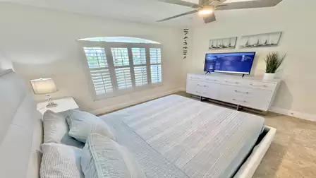 Bright bedroom with queen-size bed, TV, ceiling fan and large plantation shutters.