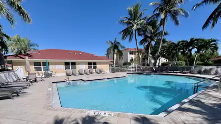 Large pool area with sun loungers, palm trees and adjacent community building