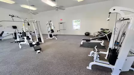 Bright fitness room with weight machines, dumbbells, and open workout space