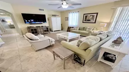Spacious living room with sofas, TV, tiled floors, and bright, comfortable furnishings