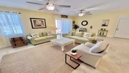 Bright, comfortable living room with two sofas, an armchair, coffee table, ceiling fans, and access to the balcony.