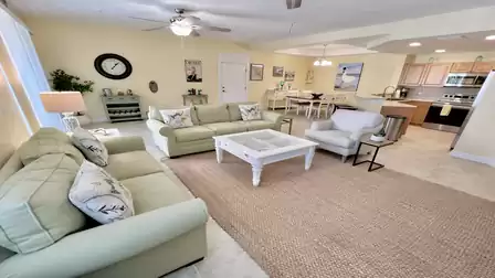 Bright open-plan living area with sofas, coffee table, area rug, and view toward the open kitchen and dining area.