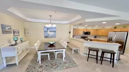 Bright dining area with dining table, chairs, and an open kitchen featuring a breakfast bar and stools.