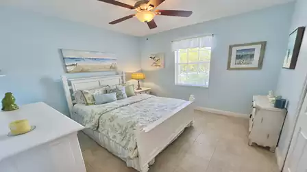 Bright bedroom with double bed, ceiling fan, bedside lamp, and window with natural light