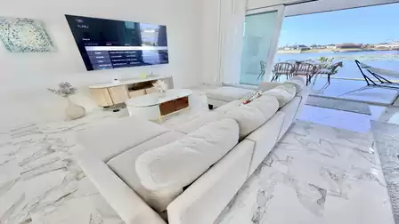 Modern living area with a spacious sectional sofa, smart TV, and direct access to the terrace with stunning waterfront views.