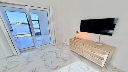 Bright bedroom with a smart TV, lake views, and direct access to the covered waterfront terrace.