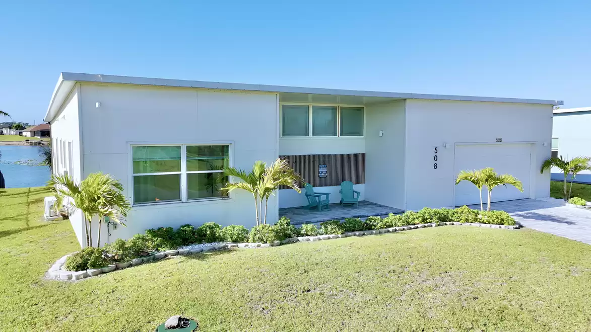 Modern vacation home on the waterfront with palm trees, landscaped garden, and covered entrance area.