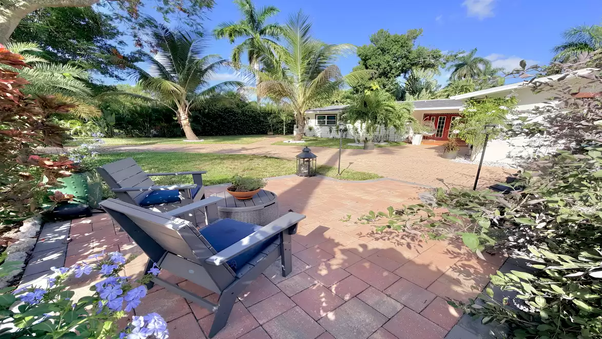 Cozy seating area in a tropical front garden with palm trees, flowering plants and views of the vacation villa in Fort Myers.
