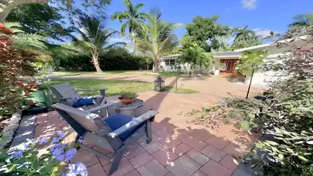 Cozy seating area in a tropical front garden with palm trees, flowering plants and views of the vacation villa in Fort Myers.