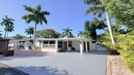 Vacation villa in Fort Myers featuring a covered carport, tropical landscaping and spacious outdoor areas beneath palm trees.