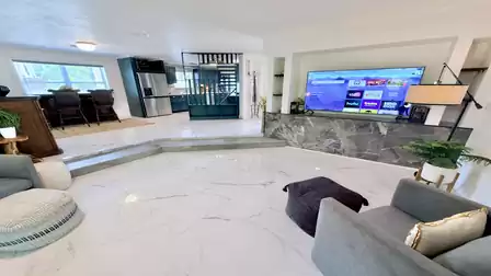 Spacious open-concept living area with a smart TV, elegant marble-style flooring, and seamless access to the modern kitchen - perfect for relaxing evenings and quality time together on vacation.