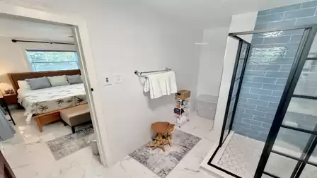 Modern bathroom with glass shower, light tiles, and direct access to the bedroom