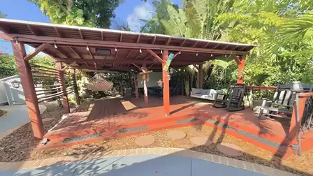 Covered wooden deck with hammock, rocking chairs, and tropical garden atmosphere