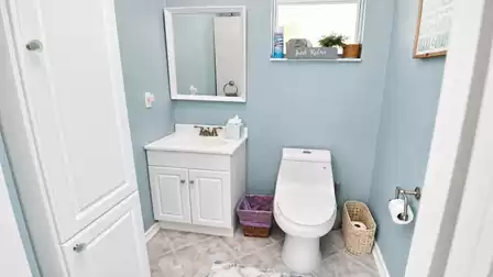 Pool bathroom with white vanity, framed mirror, toilet and baskets under small window